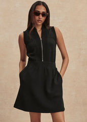 Woman wearing a black sleeveless dress with a zipper on a beige background
