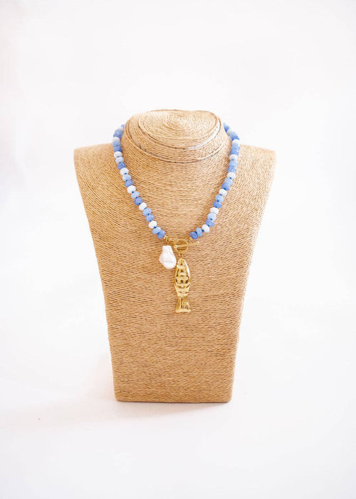 Necklace with blue beads and a gold fish pendant on a beige mannequin bust against a white background