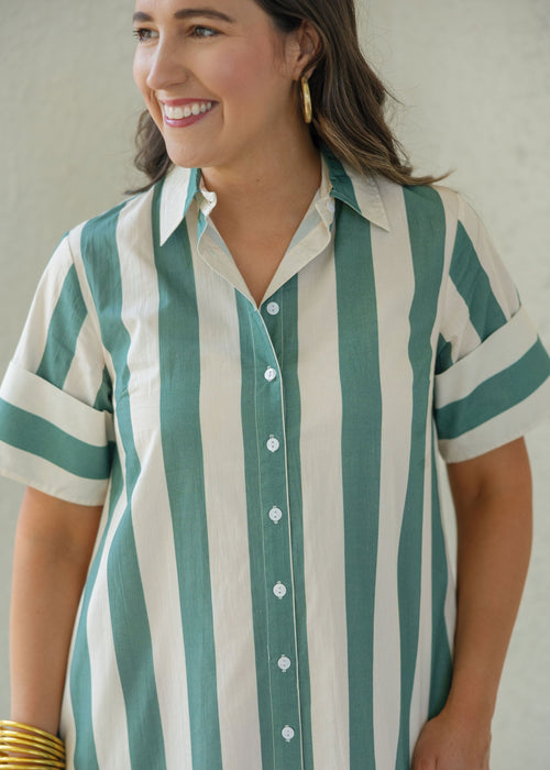 A woman wearing a short-sleeve button-front collared shirt dress with vertical mint green and off-white stripes, accessorized with gold hoop earrings and stacked gold bangles.