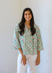 Woman wearing a floral blouse and white pants against a plain background
