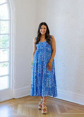 Woman in a blue dress standing in a room with white walls and wooden flooring.