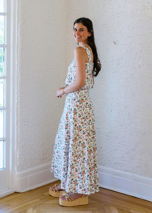Woman in a floral dress standing in a room with a large window.