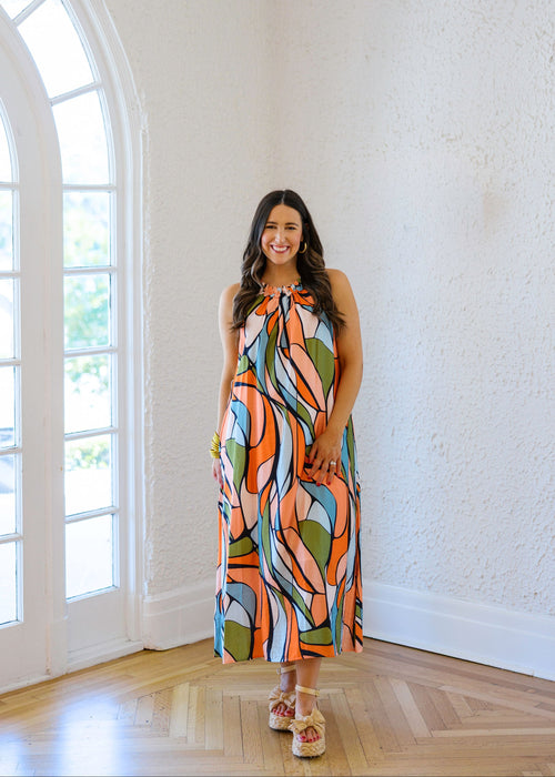 Woman wearing a colorful dress standing in a room with large windows.