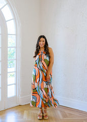 Woman in a colorful dress standing in a room with white walls and wooden flooring.