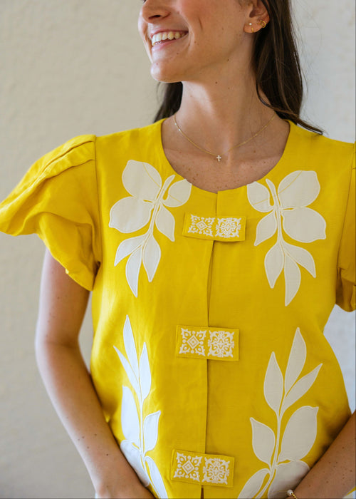 Woman wearing a yellow dress with white floral patterns against a neutral background