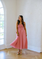 Woman in a pink checkered dress standing in a room with white walls and wooden floor.