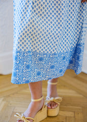 Person wearing a blue and white patterned skirt with yellow sandals on a wooden floor.