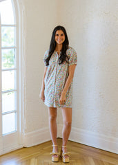 Woman in a floral dress standing in a room with a large window.