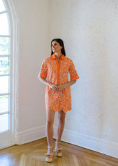 Woman wearing an orange patterned dress standing in a room with a window and wooden floor.