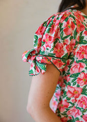 Person wearing a floral dress with pink flowers and green leaves on a plain background