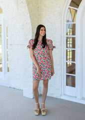 Woman in a floral dress standing in front of a white brick building with large windows.