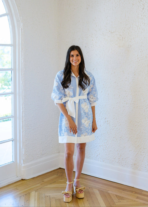 Woman wearing a light blue dress with white floral patterns in a bright room.