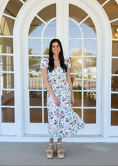 Woman in a floral dress standing in front of a large white door with glass panels.