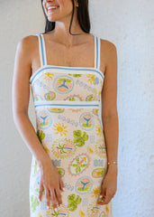 Woman wearing a colorful dress with a pattern of suns and flowers against a plain background