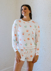 Woman wearing a white long-sleeve top and shorts with fruit pattern against a white wall.