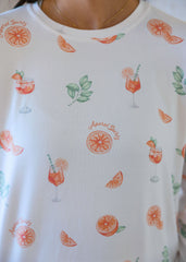 Close-up of a white shirt with orange-themed pattern including drinks, leaves, and oranges.