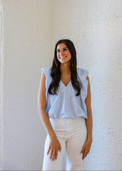 Woman wearing a light blue top and white pants against a textured white wall