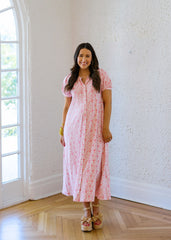Woman in a pink dress standing in a room with large windows.