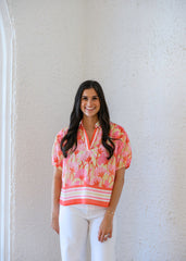 Woman wearing a colorful floral blouse against a white wall
