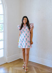 Woman wearing a pink dress with a floral pattern in a room with white walls and wooden flooring.