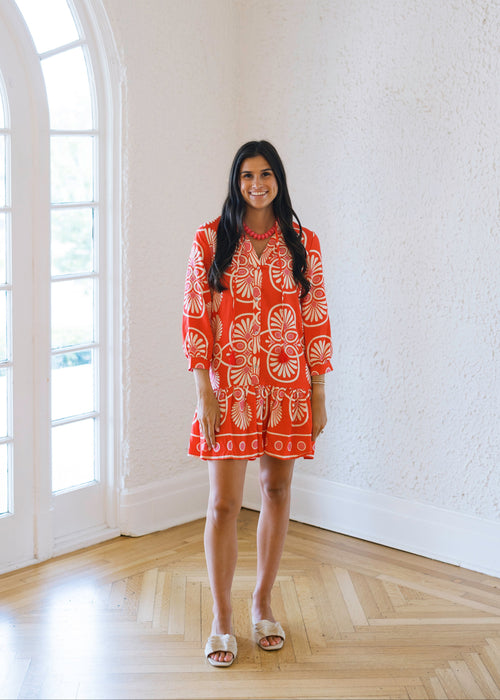 Woman in an orange dress standing in a bright room with large windows.