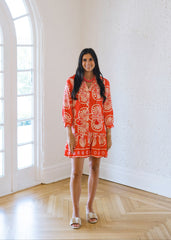 Woman in an orange dress standing in a bright room with large windows.