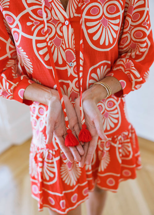Person wearing a red and white patterned dress with tassel earrings.