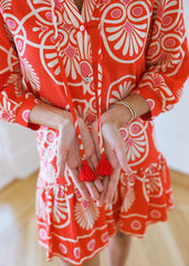 Person wearing a red and white patterned dress with tassel earrings.