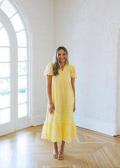 Woman in a yellow dress standing in a bright room with large windows.