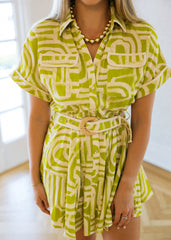 Woman wearing a green and white patterned dress with a belt in a bright room.