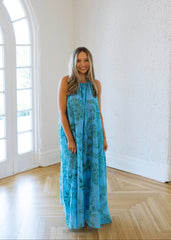 Woman in a blue floral dress standing in a bright room with large windows.