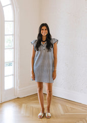 Woman in a checkered dress standing in a bright room with large windows.