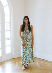 Woman in a floral dress standing in a bright room with large windows.