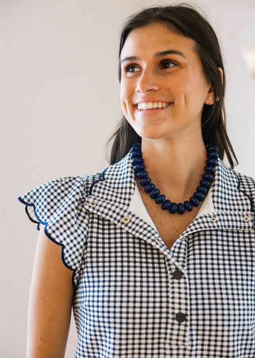 Woman wearing a blue and white checkered shirt with a necklace, smiling against a plain background