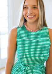 Woman wearing a green and white checkered dress with a pink necklace indoors.