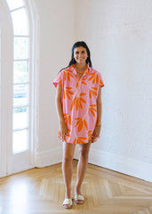 Woman wearing a pink dress with orange leaf pattern in a bright room.