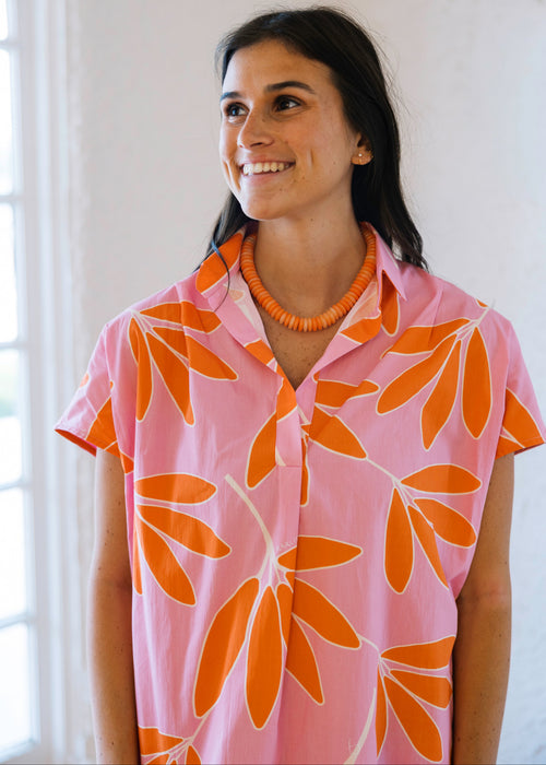 Woman wearing a pink shirt with orange floral patterns against a white wall.