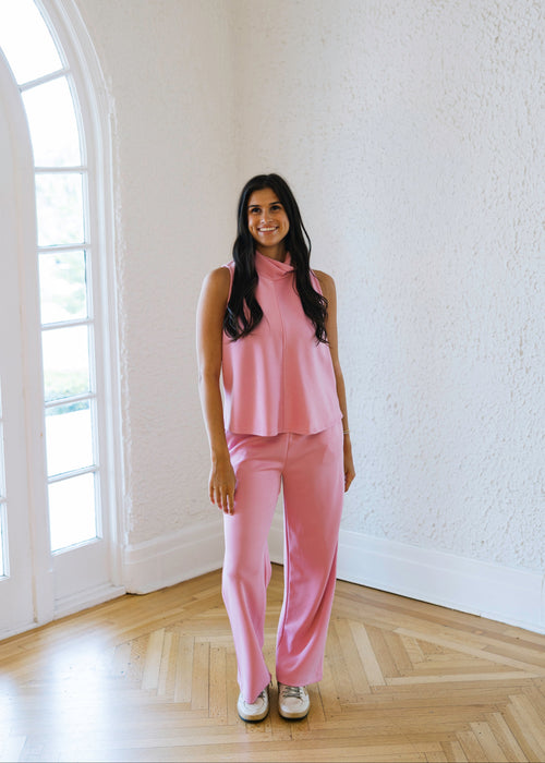 Woman in a pink outfit standing in a room with white walls and wooden flooring.