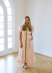Woman in a striped dress standing in a bright room with large windows.