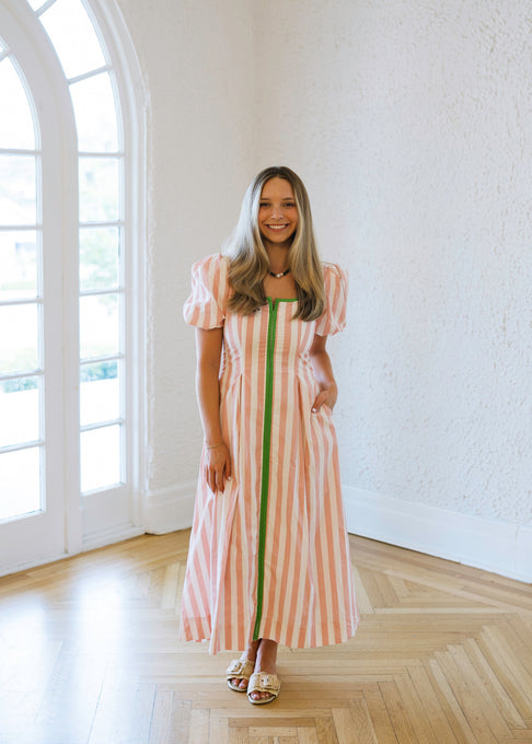 Woman in a striped dress standing in a bright room with large windows.