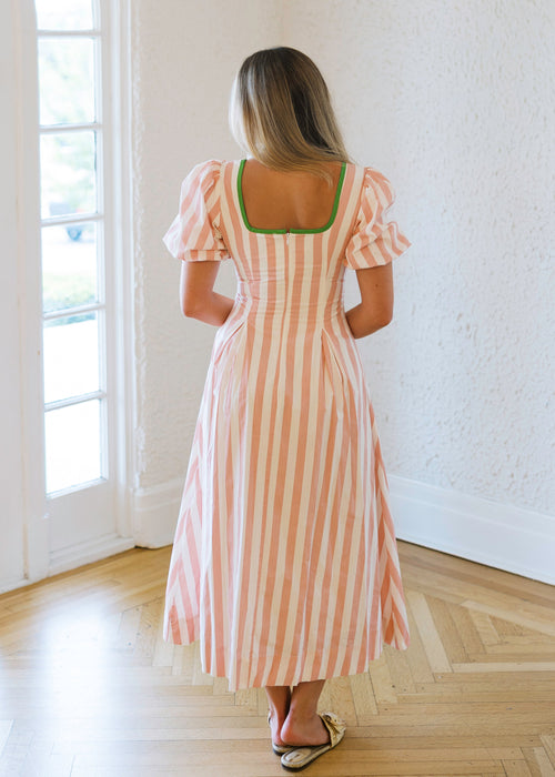 Woman in a striped dress standing in a bright room with large windows.