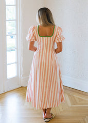 Woman in a striped dress standing in a bright room with large windows.