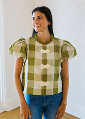 Woman wearing a green and white checkered shirt with puffed sleeves in a bright room.
