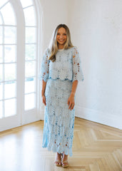 Woman in a light blue lace dress standing in a bright room with large windows.