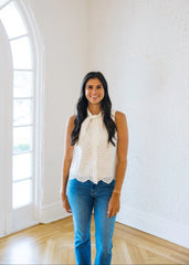 Woman wearing a white lace top and blue jeans standing in a bright room with large windows.