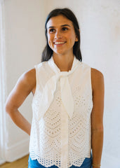 Woman wearing a white lace top with a bow tie against a white wall.