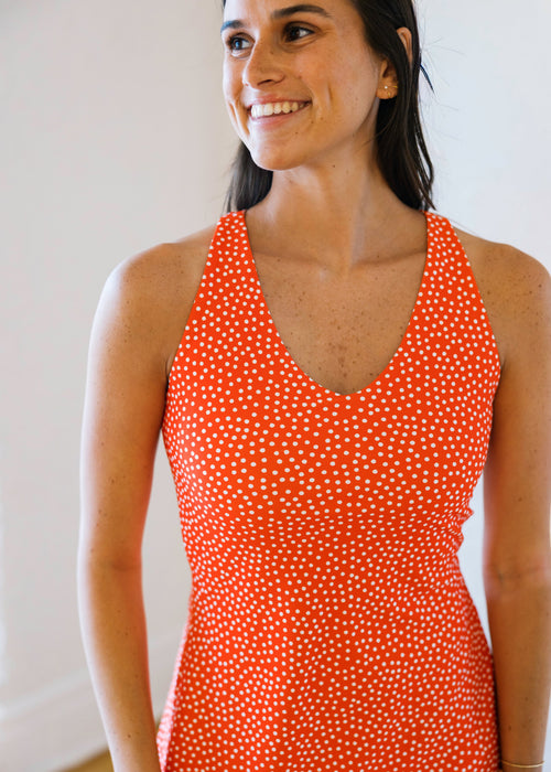 Woman wearing an orange polka dot dress against a plain background