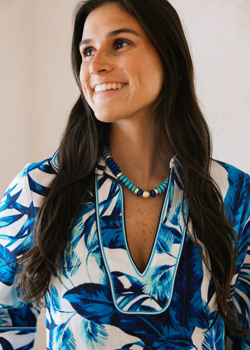 Woman wearing a blue and white floral dress with a necklace against a plain background