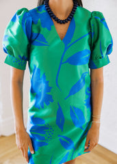 Person wearing a green and blue floral dress with puffed sleeves against a white background