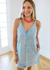 Woman wearing a light blue denim dress with a red necklace indoors.